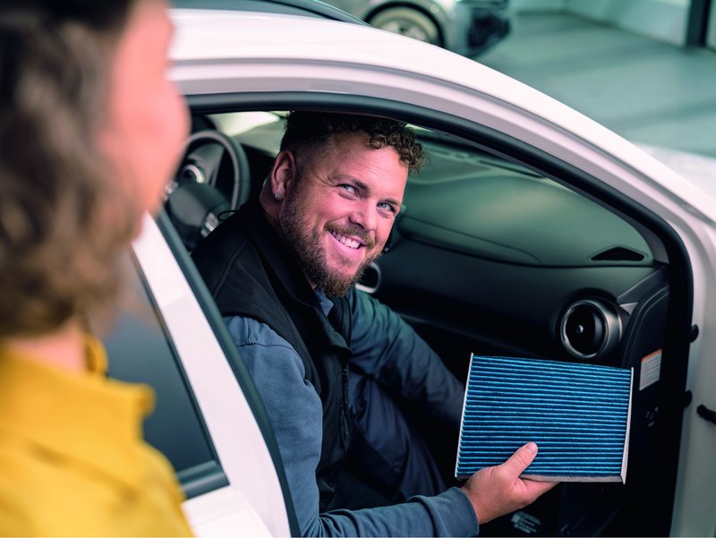 wechsel-innenraumfilter.jpg Mann der im Auto sitzt und einen Innenraumfilter in der Hand hält.